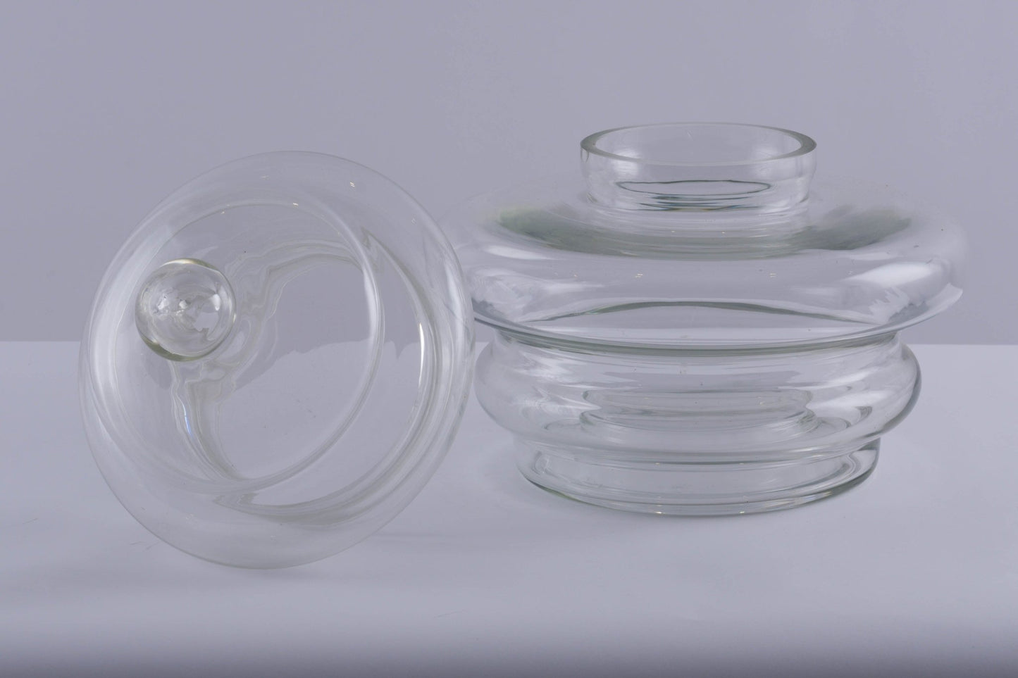 Large clear glass jar vessel with round ball handle lid and tapered tubular shape on a white surface