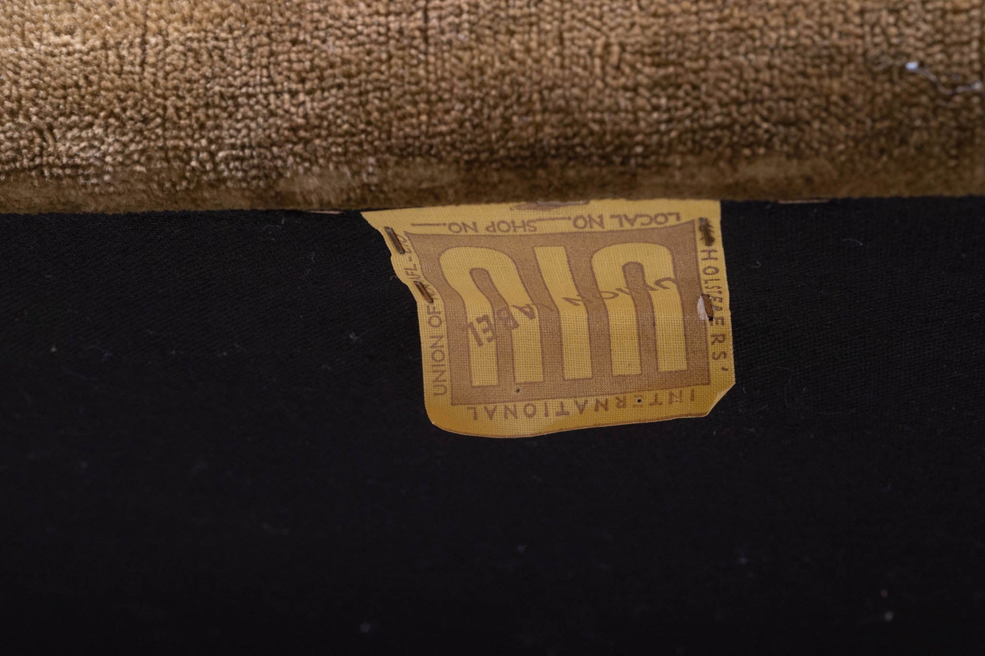 Close-up of vintage fabric label on underside of mid-century settee with textured upholstery in brown tones