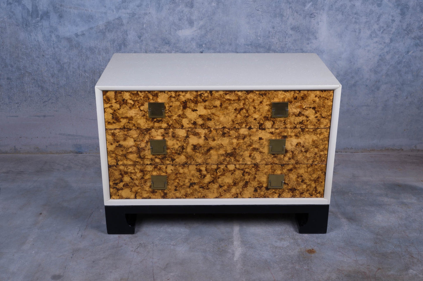 Three-drawer faux tortoiseshell dresser with white riveted body and black lacquered base with carved feet.