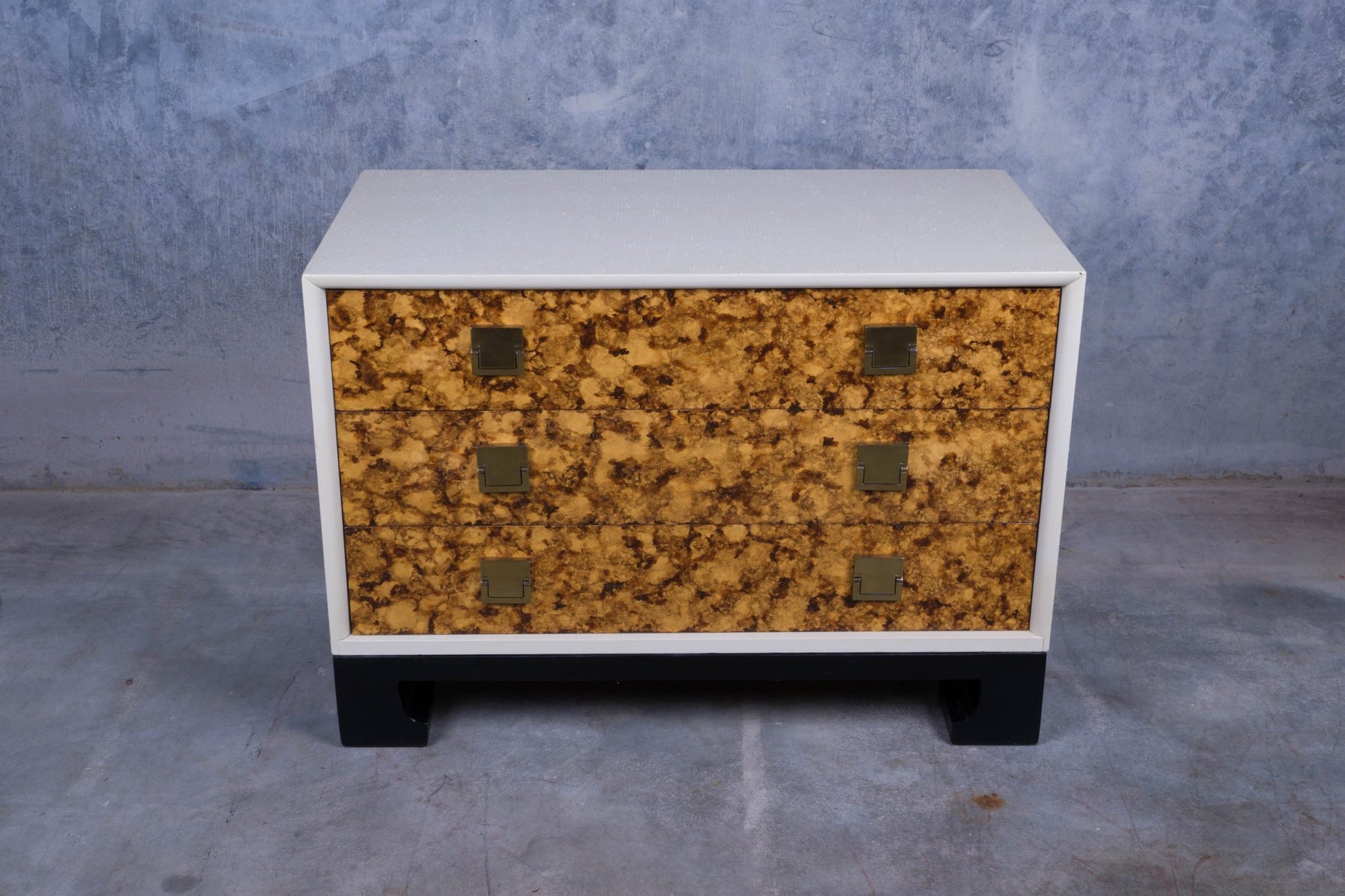 Three-drawer faux tortoiseshell dresser with white riveted body and black lacquered base with carved feet.