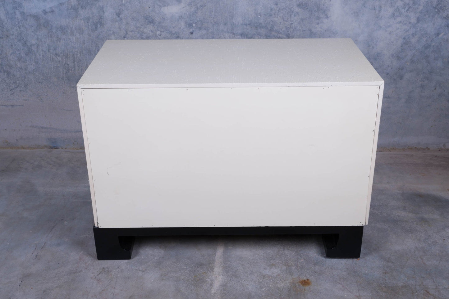 White faux tortoiseshell three-drawer cabinet with white riveted exterior and black lacquered carved base on concrete floor
