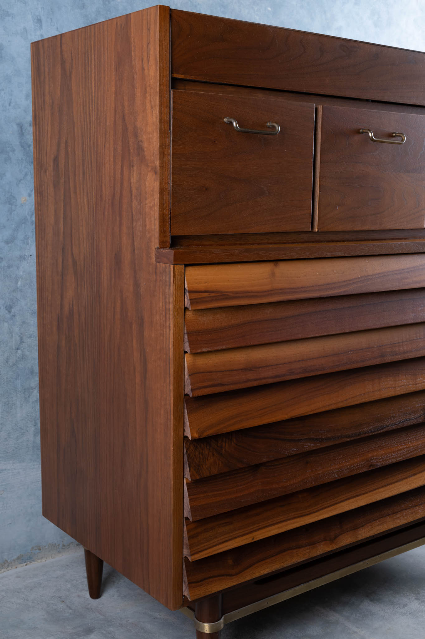 Mid-century modern walnut dresser with louvered drawers, brass handles, tapered legs, and clean minimalist design.