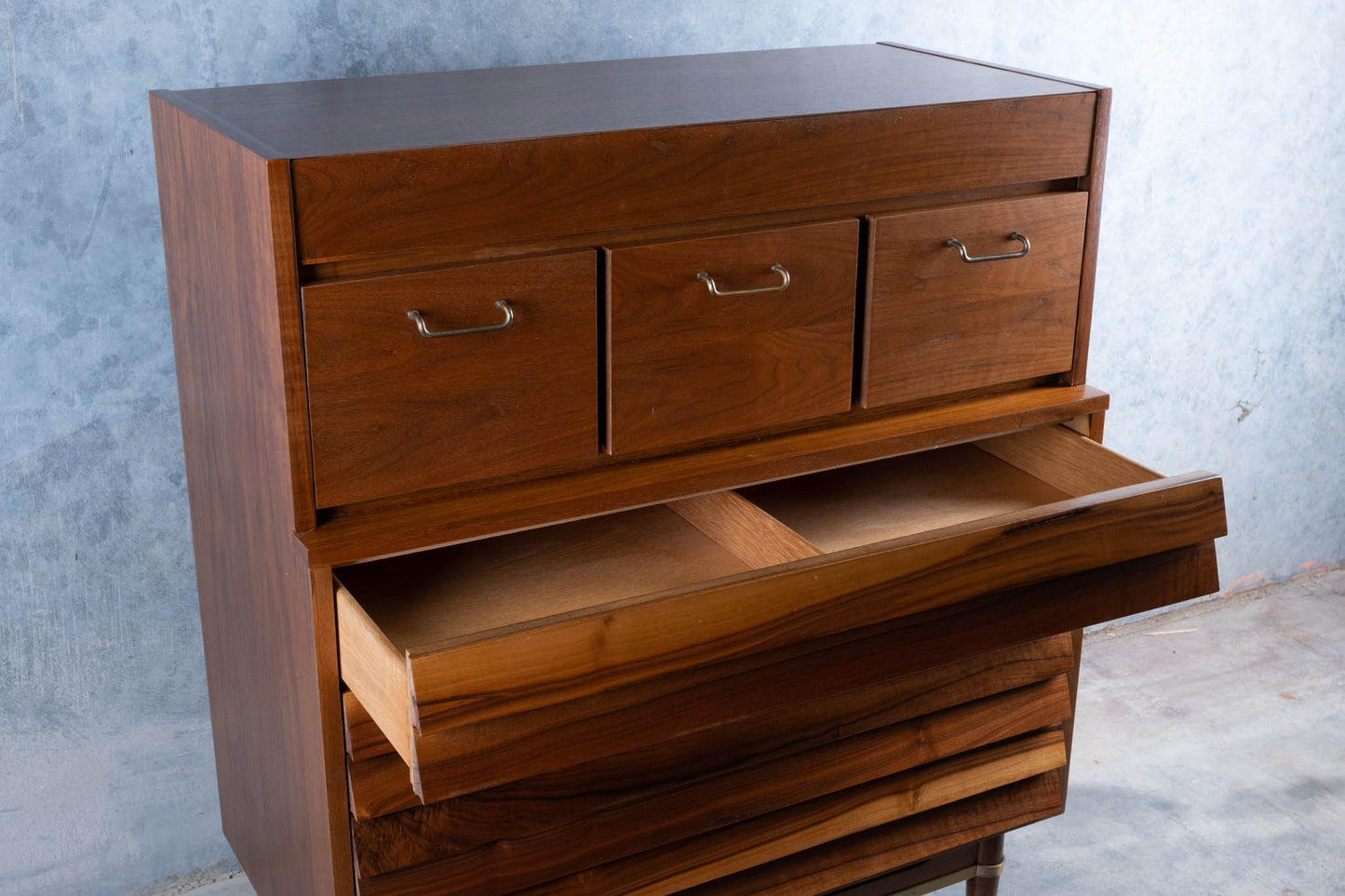 Mid-century modern walnut highboy dresser by Merton L. Gershun with seven drawers and brass handles on gray background.
