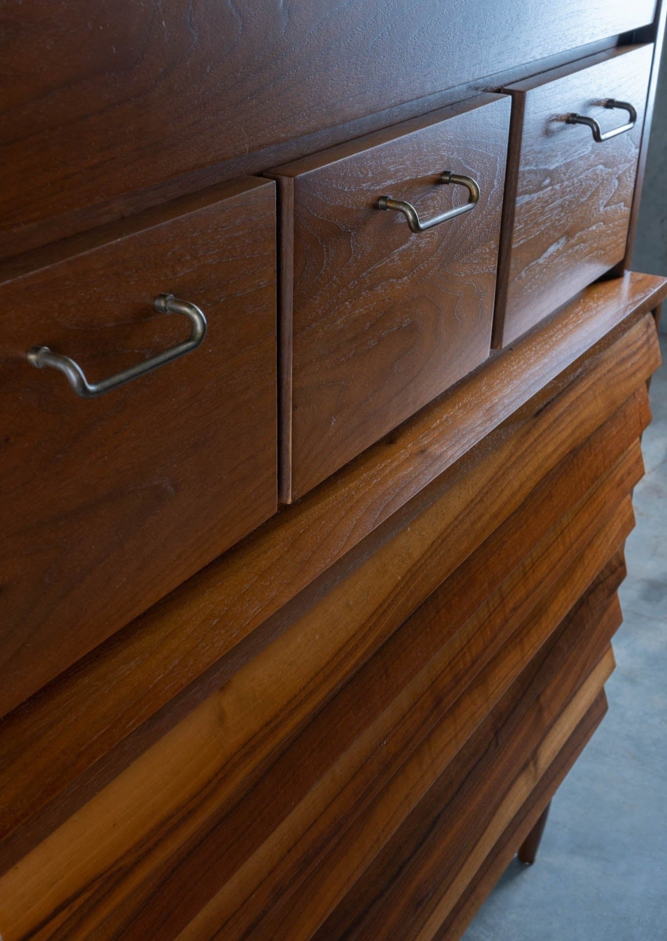 Close-up of mid-century modern walnut dresser drawers with metal handles and louvered wooden front panel design
