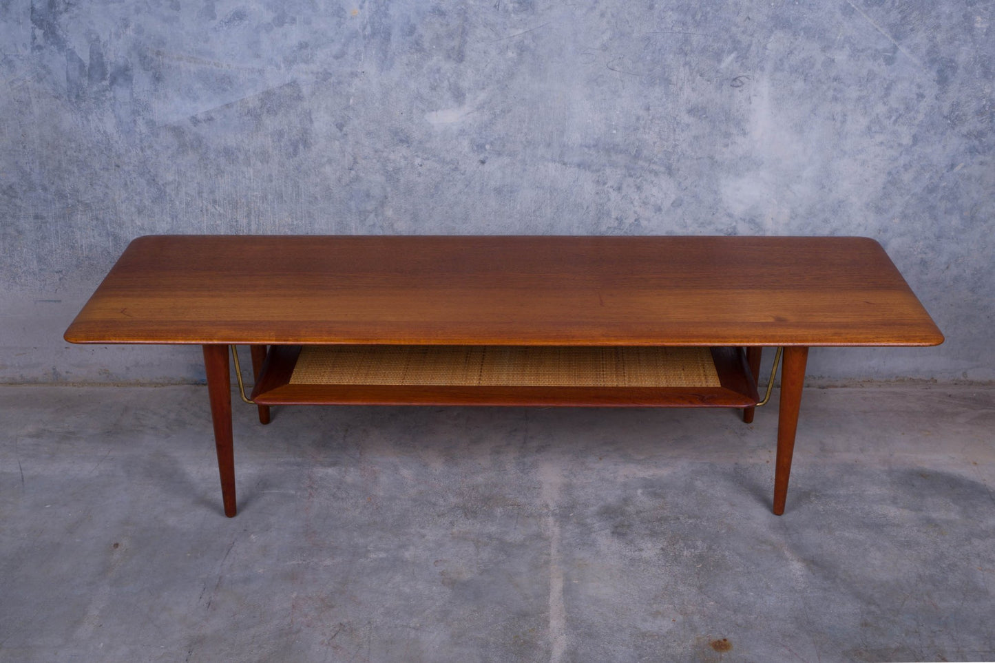 1950s Danish teak coffee table with cane shelf, tapered legs, and minimalist mid-century modern design on concrete floor
