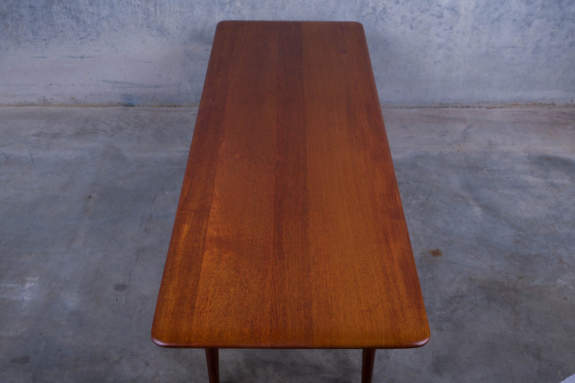 Mid-century modern teak coffee table with rectangular top and clean lines on concrete floor background