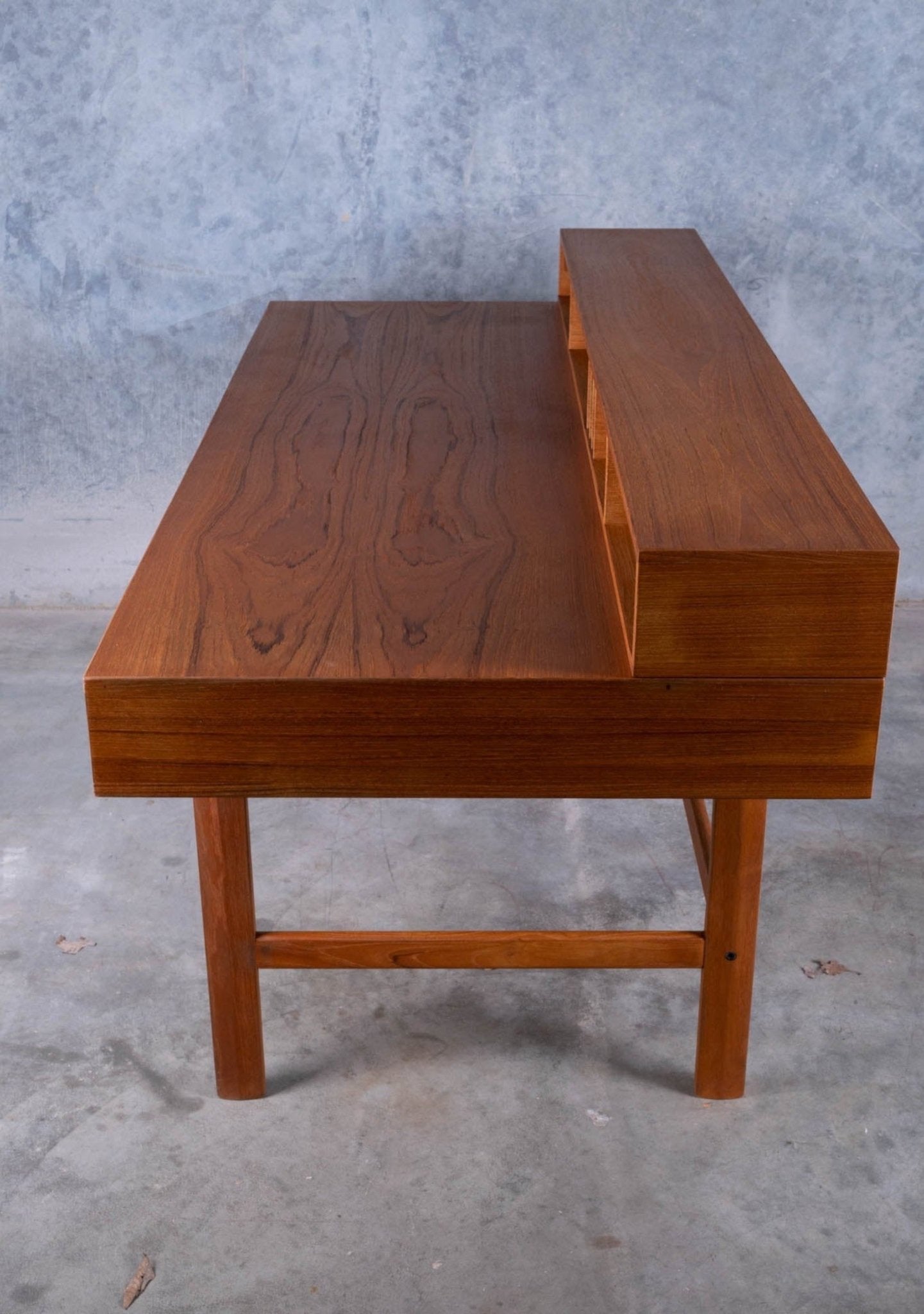 Minimalist mid-century modern rosewood desk with raised back shelf and clean rectangular design on concrete floor.