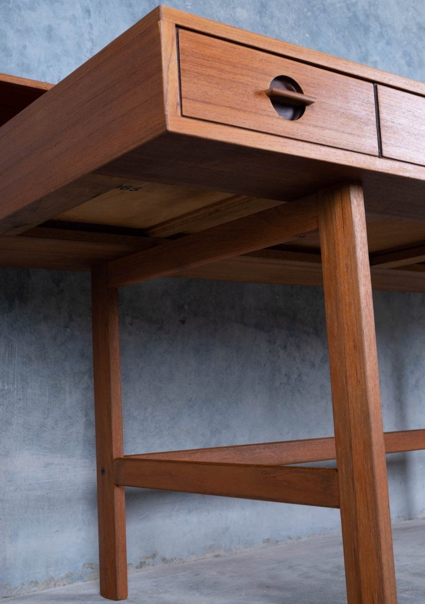 Close-up of mid-century modern rosewood desk leg and drawer with circular cutout handle against textured gray wall background