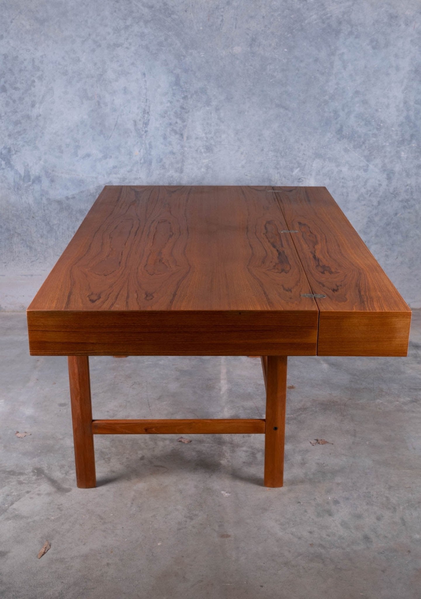 Mid-century modern rosewood flip-top desk by Jens Quistgaard, featuring clean lines and sturdy wooden legs on concrete floor.