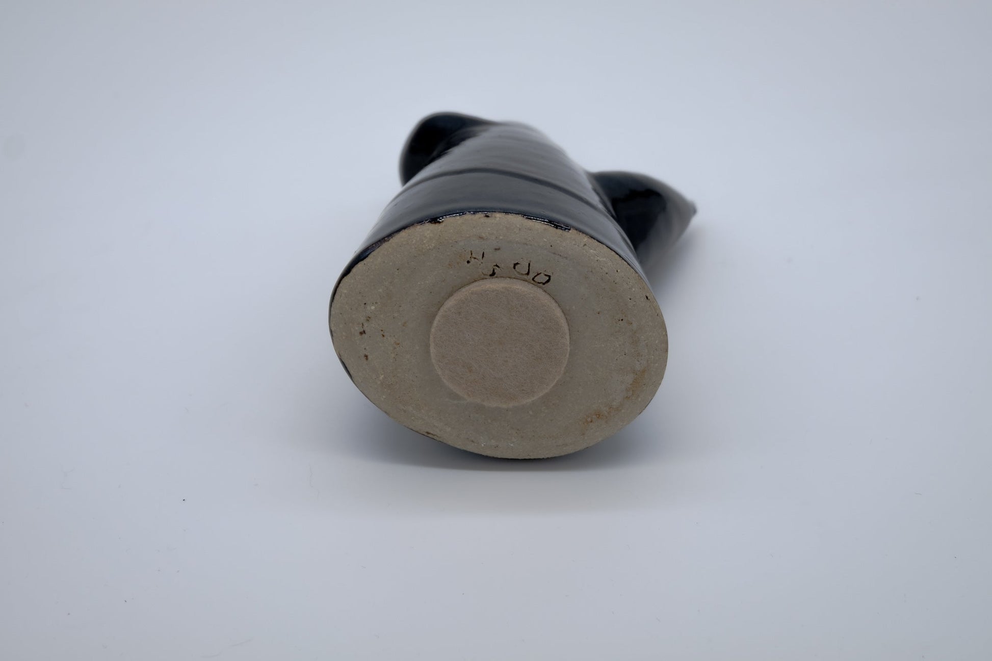 Base view of a black studio pottery vase with a rounded bottom and maker’s mark on a white background