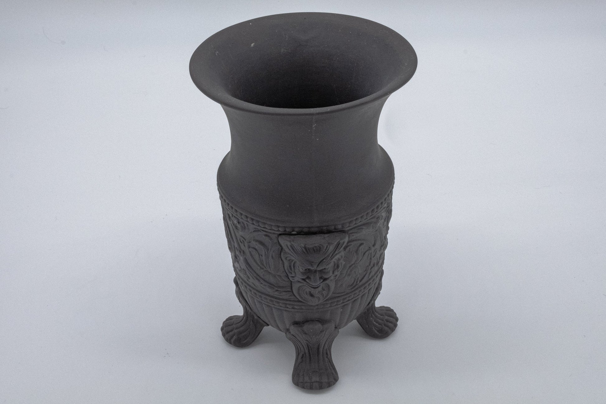 Wedgwood black basalt vase with carved Greek god portraits and stylized designs on tripod feet against white background