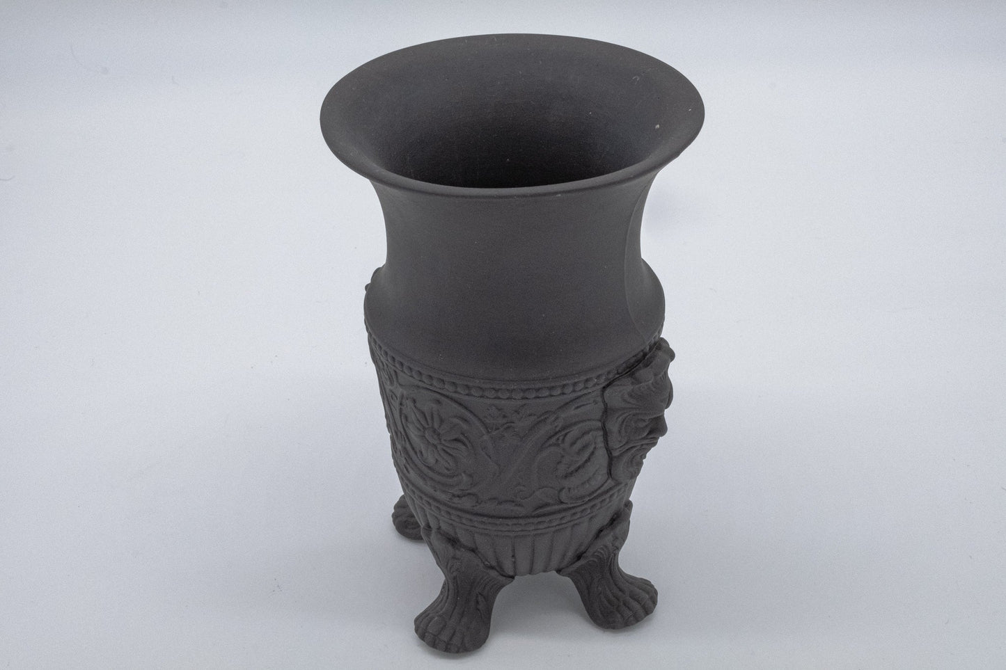 Wedgwood solid black basalt vase with carved Greek god portraits and stylized flowing decorative details on feet