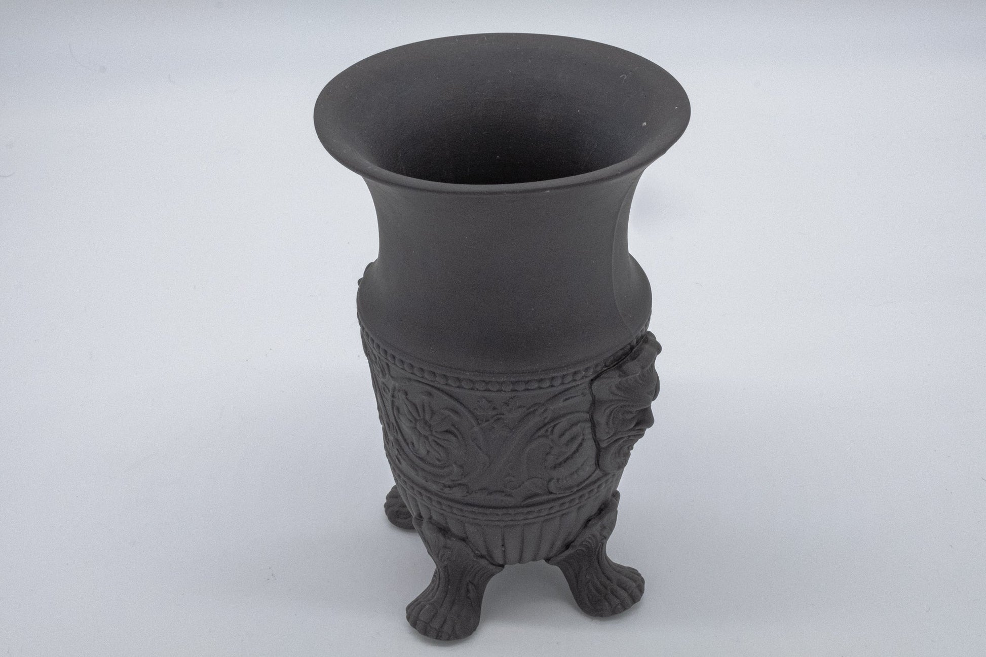 Wedgwood solid black basalt vase with carved Greek god portraits and stylized flowing decorative details on feet